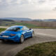Blue Alpine sports car parked on a rural road with green fields and rolling hills in the background.